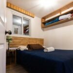 A cozy bedroom featuring a comfy bed, wooden shelves, and natural light.
