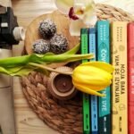 Top view stack of books on table near beautiful yellow tulip and orchid flowers arranged with chocolate truffles placed on wicker placemat
